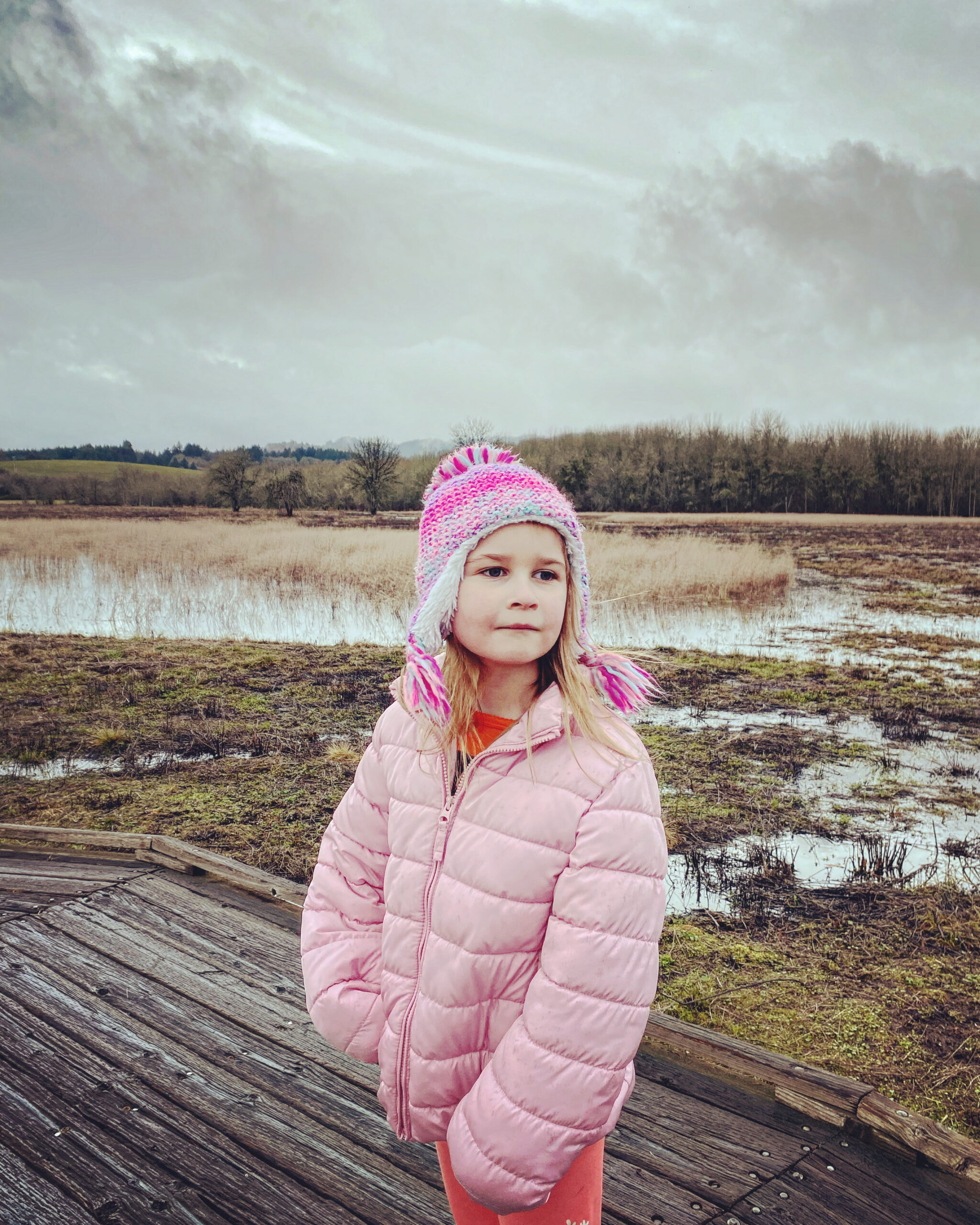 A six year old blonde girl smiles absentmindedly as she stands on a wood planked path over the wetlands.