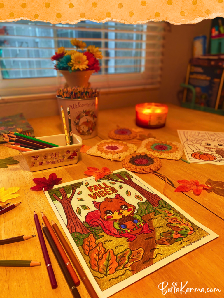 An autumn display decorates a yellow kitchen table. Colored pencils in fall hues surround a coloring page of a cute squirrel in the forest holding a chestnut with the words "Fall Vibes" above his head.