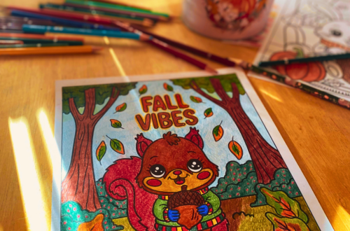 An autumn display decorates a yellow kitchen table. Colored pencils in fall hues surround a coloring page of a cute squirrel in the forest holding a chestnut with the words "Fall Vibes" above his head.